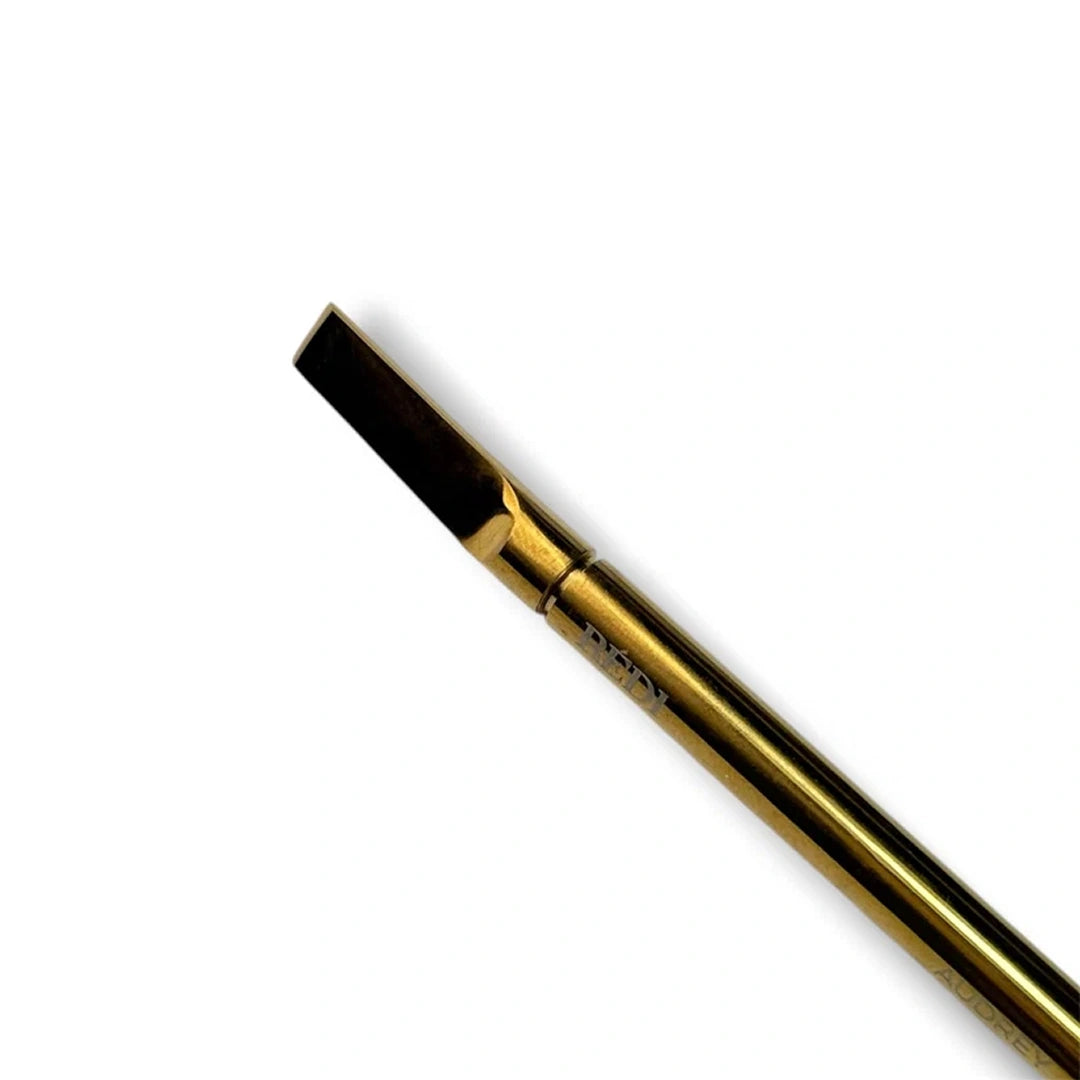 A close-up of a gold metal tip with a dark bristle head, shown diagonally on a plain white background.